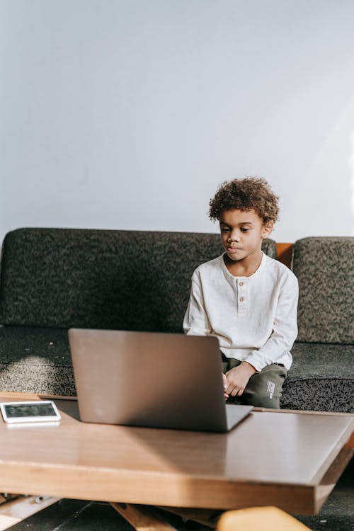 Contemplative African American boy browsing netbook and pondering at table in comfortable lounge in daytime