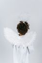 Back view of anonymous African American child pretending angel in white costume with wings and nimbus on white background