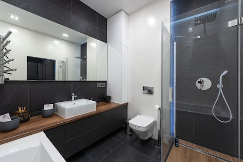 Interior of contemporary washroom with modern transparent shower cabin placed near toilet and sink at mirror with reflection of room
