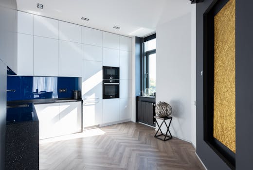 Interior of contemporary light kitchen with white cupboards and oven placed near window and decorations in room with modern decorations