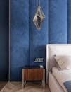 Part of comfortable bed with cushions and blanket placed near blue wall and bedside table in modern bedroom with hanging decoration