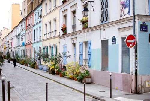 Free A picturesque street in Paris, featuring pastel-colored buildings and vibrant potted plants. Stock Photo