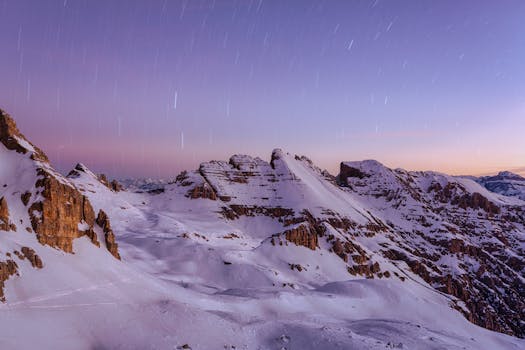 Breathtaking view of the snow-covered Dolomites under a purple twilight sky with star trails.