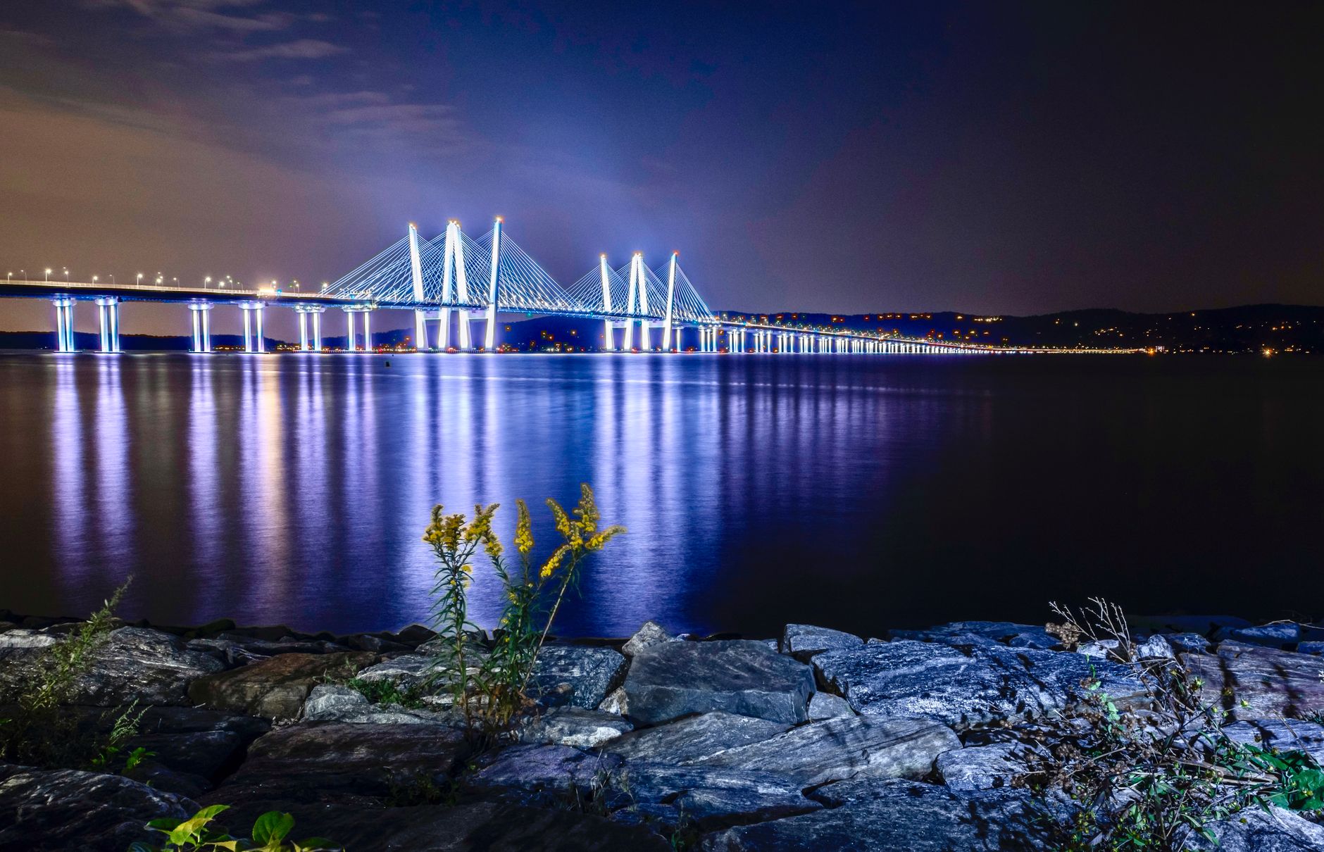 Stunning night view of the illuminated Tappan Zee Bridge over the Hudson River with reflections on the water.