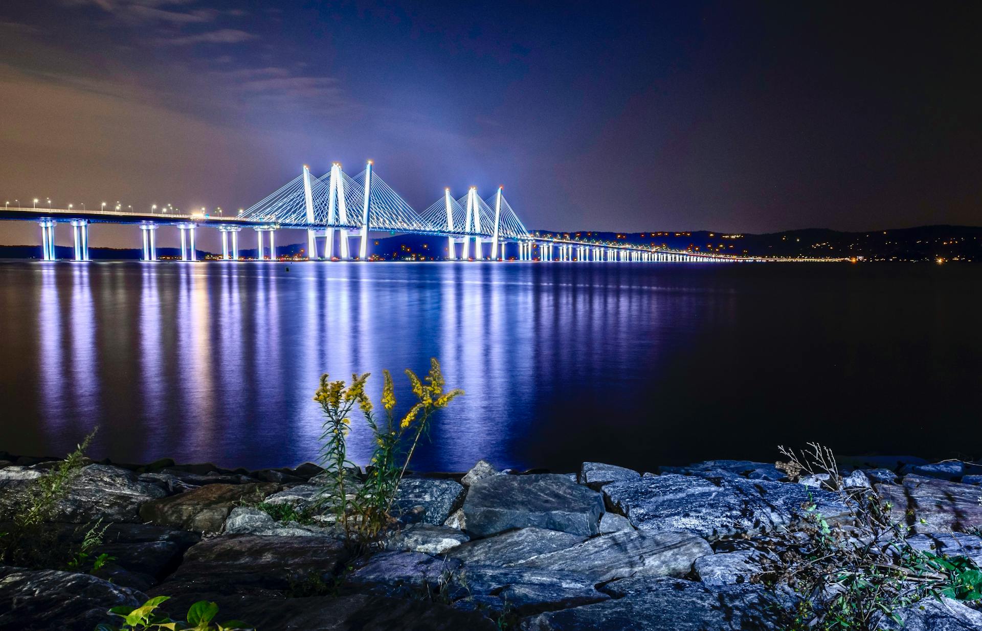 Stunning night view of the illuminated Tappan Zee Bridge over the Hudson River with reflections on the water.