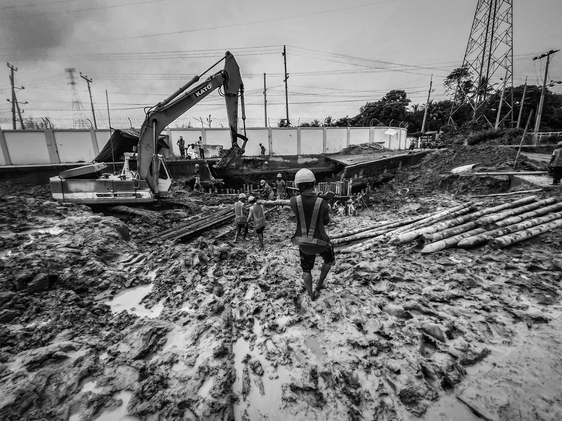 Men working on a muddy construction site with excavator in action.