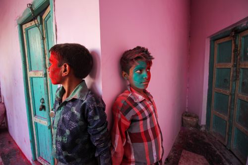 Free Colorful celebration of Holi Festival with two boys covered in vibrant face paint leaning against a pink wall. Stock Photo