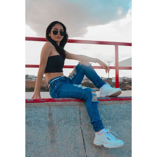 A Woman in Denim Pants Sitting on Concrete Wall 