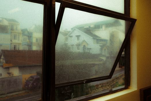A moody view through a wet window showcasing the misty streets and architecture of Dalat, Vietnam.