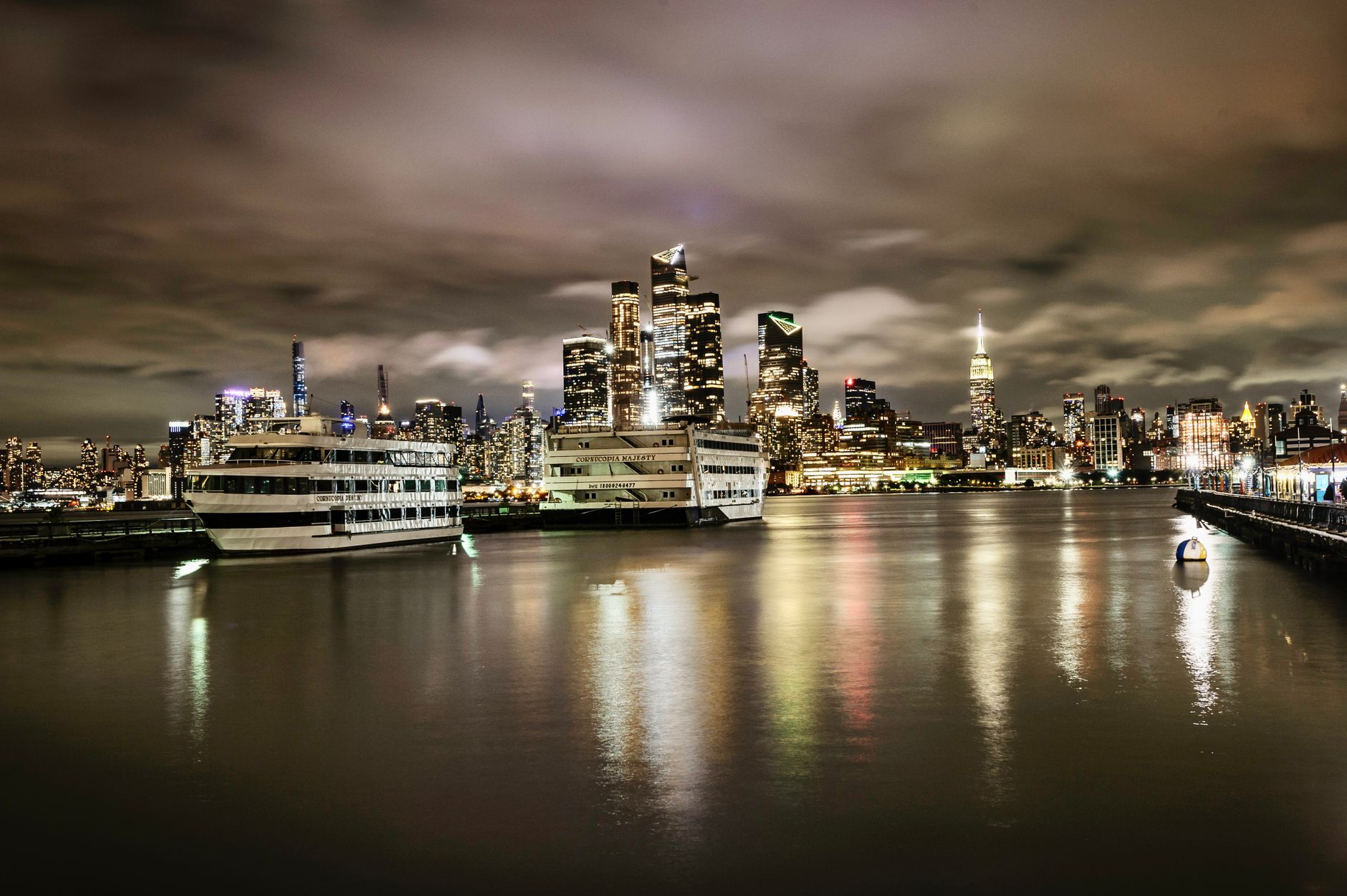 Stunning nighttime view of Midtown Manhattan skyline from Hoboken waterfront with boats and reflections.