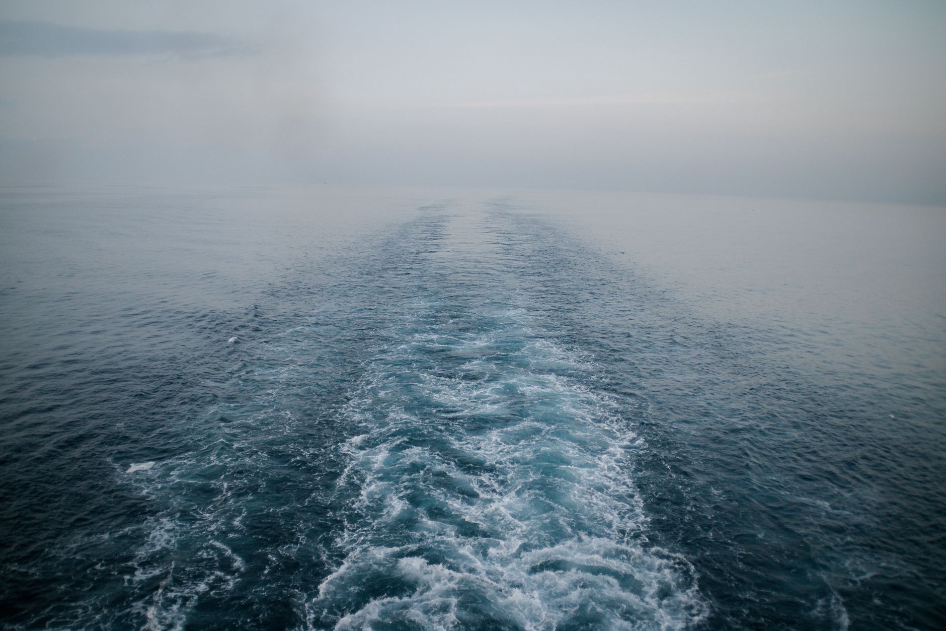 A serene seascape showing a boat wake disappearing into foggy horizon, captured at day.