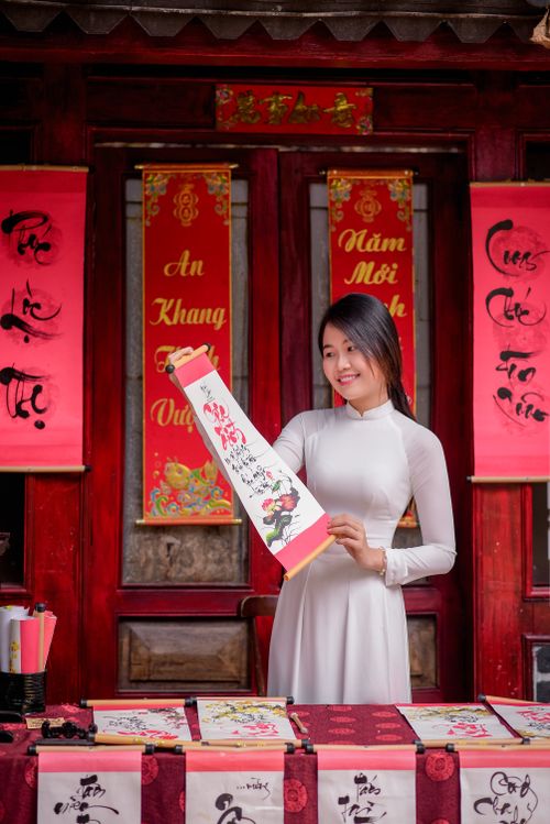 Free A woman in traditional attire showing vibrant Vietnamese calligraphy scrolls outdoors. Stock Photo