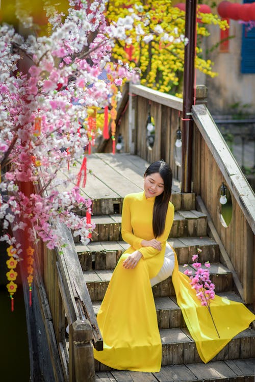 Free Woman in Yellow Ao Dai Dress Sitting on Wooden Staircase  Stock Photo