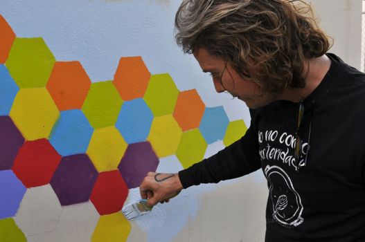 A man paints a vibrant hexagonal mural in Caguas, showcasing artistic creativity.
