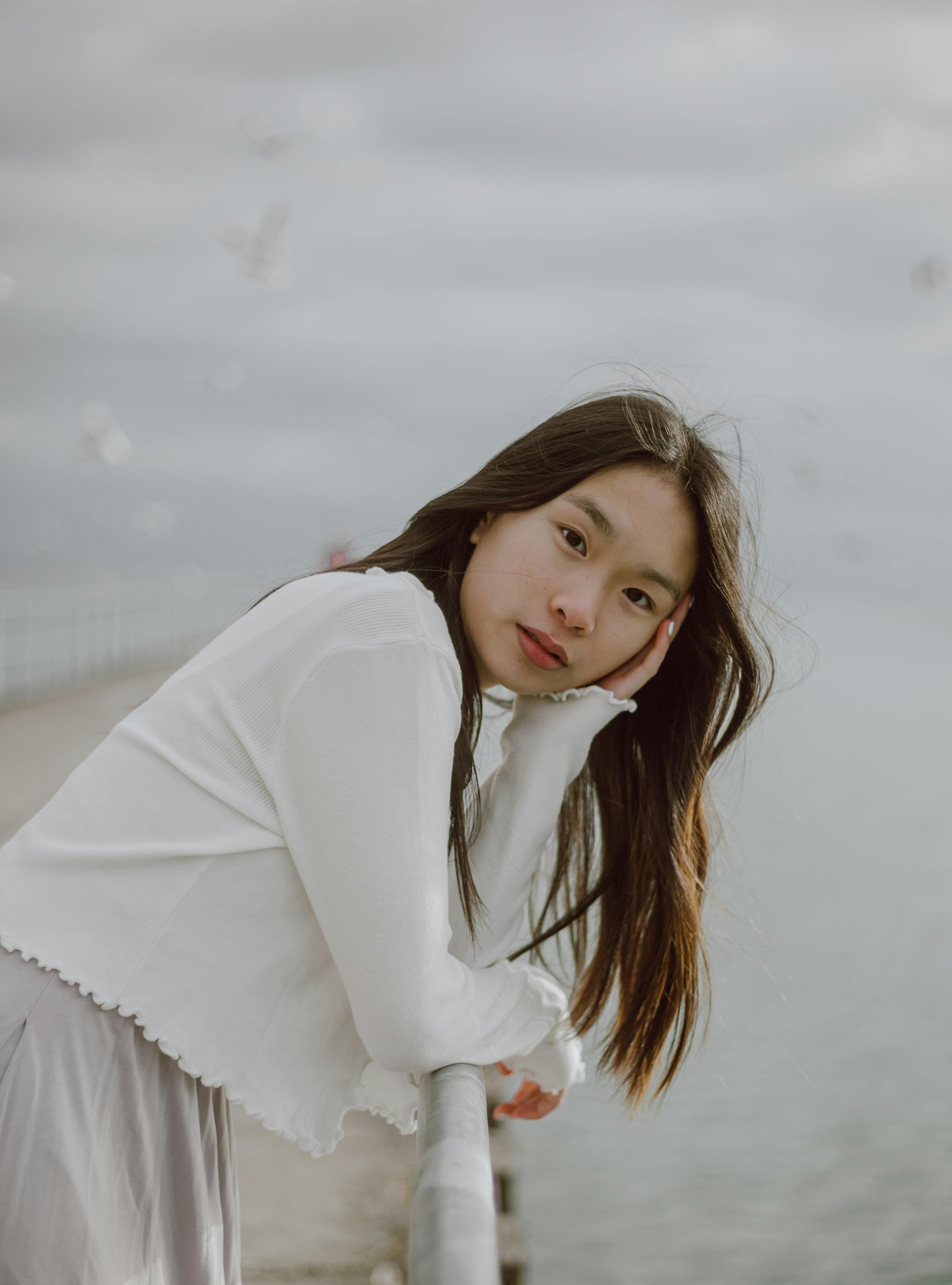 Side view of young gentle ethnic female tourist leaning with hand on fence against ocean and looking at camera