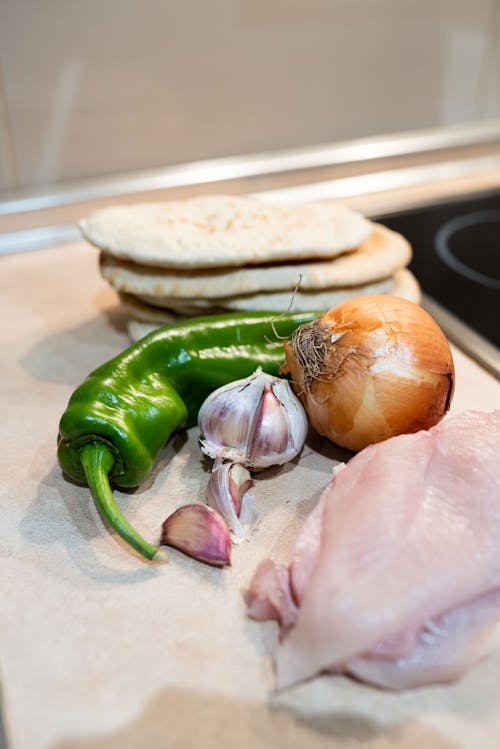 Fresh vegetables with pita bread and chicken fillet placed on table in kitchen