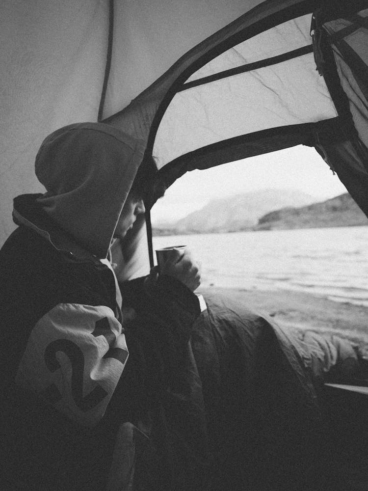 Pensive Young Guy Drinking Hot Beverage In Tent On Seashore