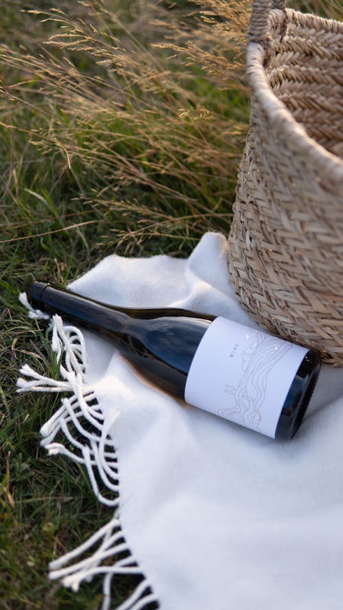 Free Wine bottle and basket placed on plaid during picnic in nature Stock Photo