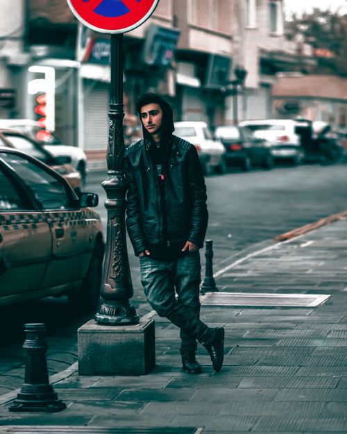 Free Stylish man in Tabriz, Iran, leans on street post wearing leather jacket. Street scene captures urban fashion vibe. Stock Photo