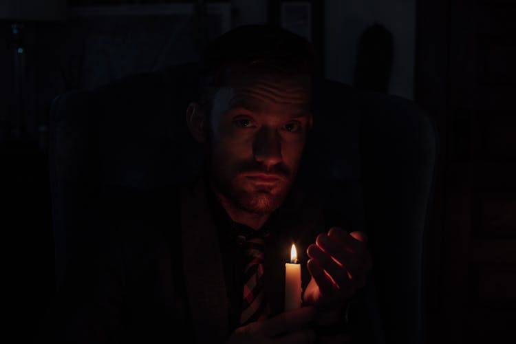 Thoughtful Young Man With Burning Candle In Hand Resting In Darkness