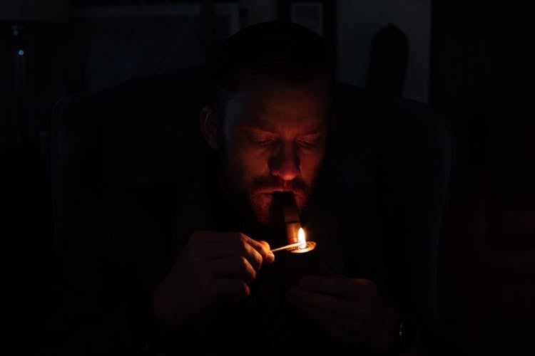 Young Man Lighting Smoking Pipe In Darkness