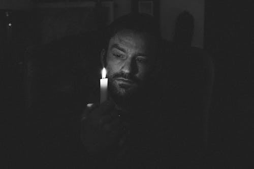 Black and white of adult bearded male looking at glowing flame of wax candle