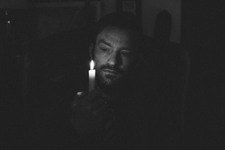 Unshaven Man With Shiny Candle In Darkness