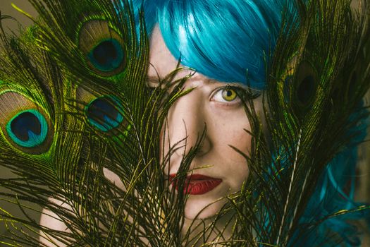 Striking portrait of a woman with vivid blue hair and peacock feathers, showcasing colorful and artistic expression.