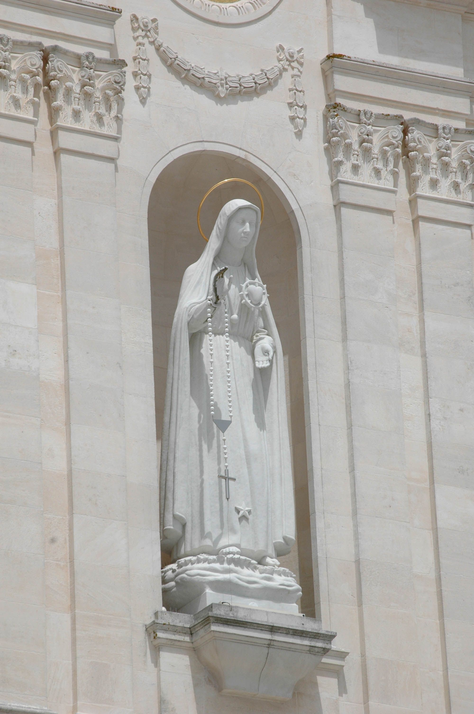 Marble statue of the Virgin Mary on a historic architectural facade, displaying intricate details.