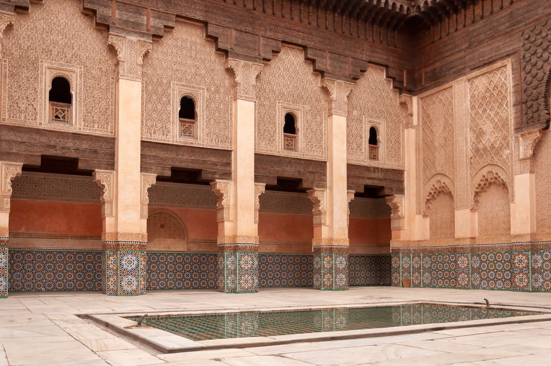 Best Places to Travel in the World 10 Main courtyard of ancient Ben Youssef Madrasa with arched passage and walls decorated with arabesque ornaments on sunny day in Marrakesh