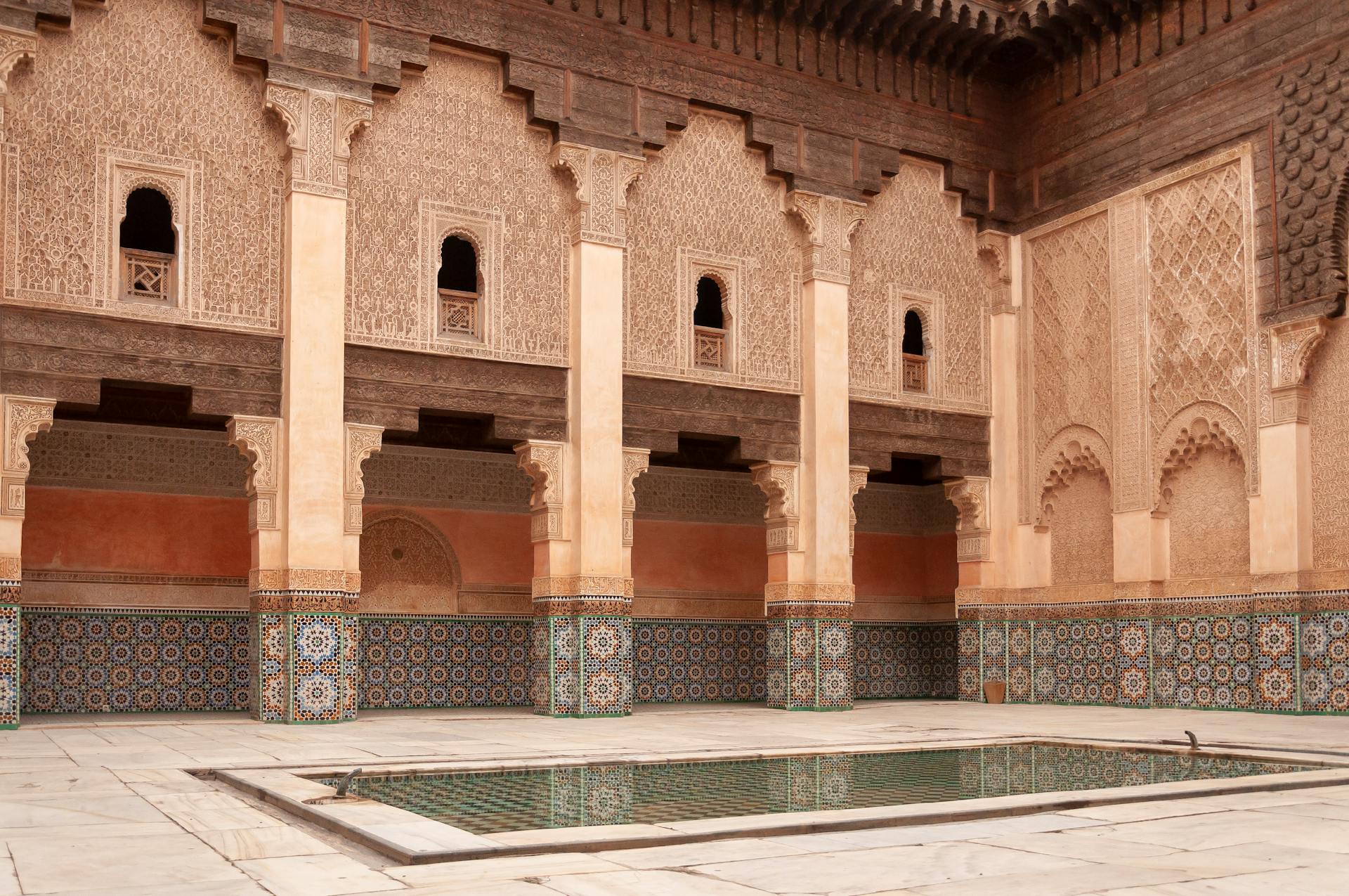 Main courtyard of ancient Ben Youssef Madrasa with arched passage and walls decorated with arabesque ornaments on sunny day in Marrakesh