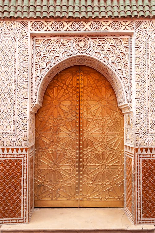 Free Ornamental arched wooden door of traditional Moroccan house with wall covered with arabesque decoration on sunny day Stock Photo
