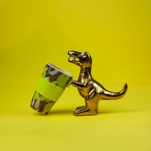 Free Golden dinosaur figurine playfully holding a decorative, eco-friendly cup on a vibrant yellow background. Stock Photo