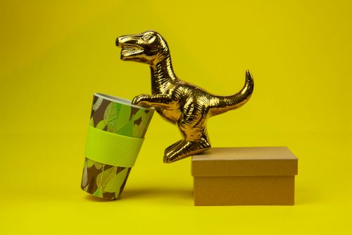 Free A golden dinosaur figurine next to a decorative cup and cardboard box, set against a vibrant yellow background. Stock Photo