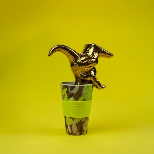 Free A shiny gold dinosaur figurine placed inside a decorative patterned cup against a vibrant yellow background. Stock Photo