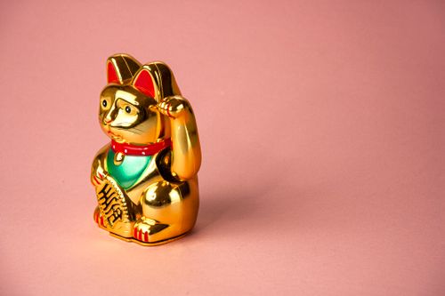 Free A gold Maneki Neko figurine symbolizing good fortune, set against a soft pink backdrop. Stock Photo