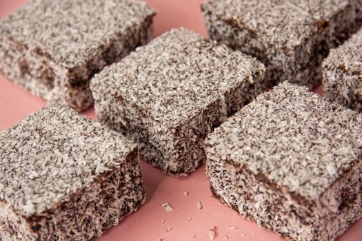 Close-up of scrumptious Australian lamingtons covered in coconut on a pastel pink surface.
