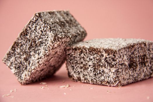 Close-up of delectable lamingtons with coconut flakes and chocolate icing on a pink background.