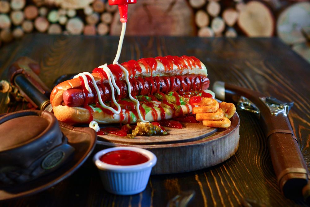 A hot dog loaded with sauces and toppings served on a wooden board