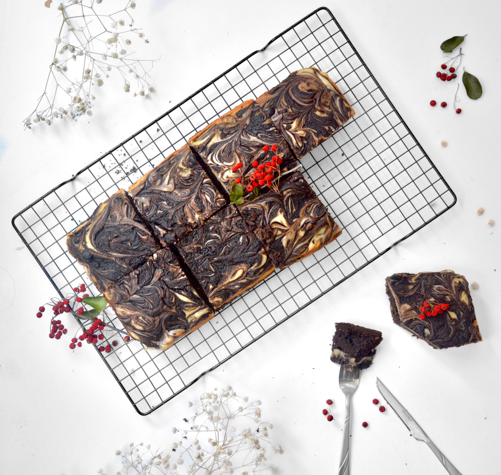 Top view of appetizing chocolate brownie cut into squares and decorated with ripe berries placed on metal grid on table