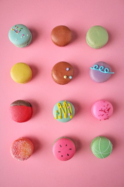 A vibrant assortment of French macarons in various colors and designs on a pink background.