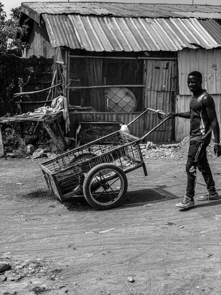 Man Pushing A Cart With Two Wheels Through A Village 