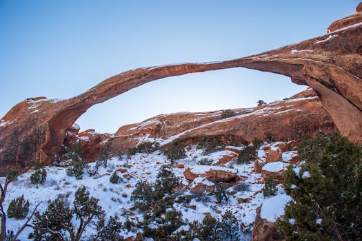 Majestic natural arch towering above snowy landscape under clear blue sky.
