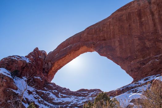 Stunning view of a sunlit arch at Arches National Park, Utah, with snow-capped surroundings.