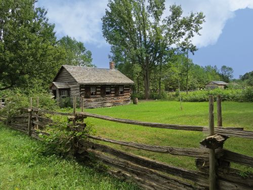 Free A charming wooden farmhouse surrounded by lush greenery and rustic fences. Stock Photo