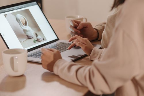 Free Two individuals reviewing a photo on a laptop, enjoying coffee indoors. Stock Photo
