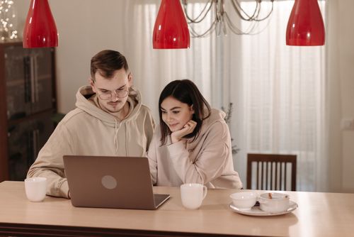 Free A couple in casual hoodies using a laptop at home, smiling and relaxed. Stock Photo