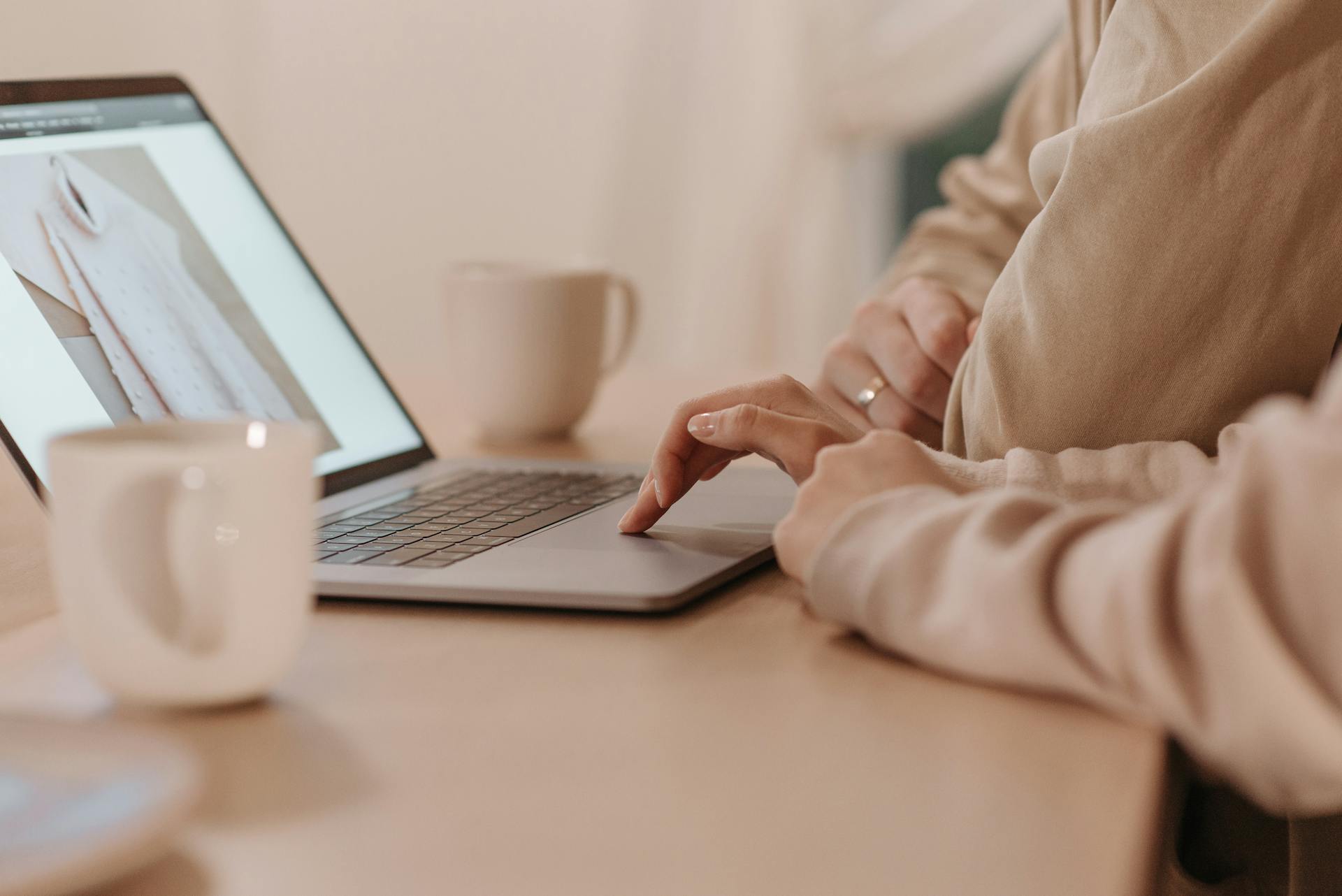 Warm indoor setting featuring a person shopping online on a laptop with a hot drink nearby.