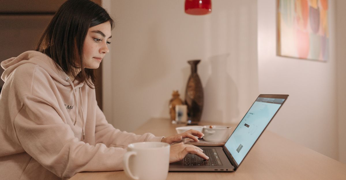 person working on laptop at kitchen table with coffee cup