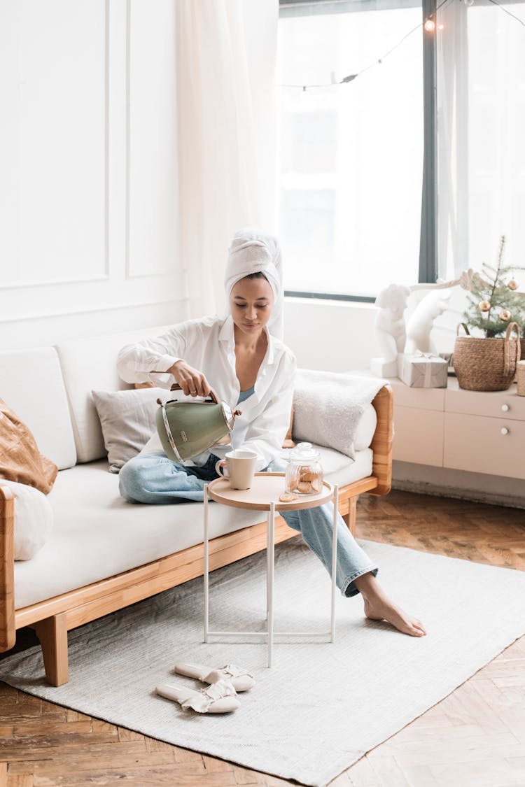 Woman With Towel Wrapped On Head Sitting On Couch Holding A Kettle